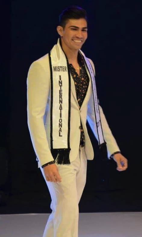 Robin Balses on stage in a white suit and the Mister International sash